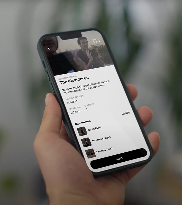 A phone held in one hand showing the Kickstarter workout, a 30 minute full body circuit above its movement list