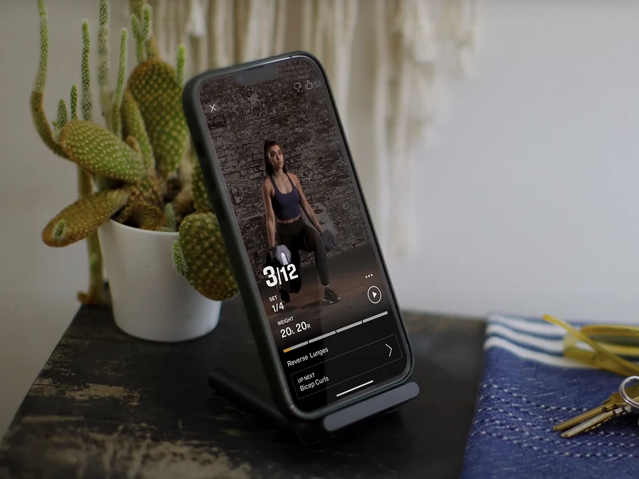 A phone on a desk stand playing a Kabata workout, set 3 of 12 reverse lunges at 20 pounds