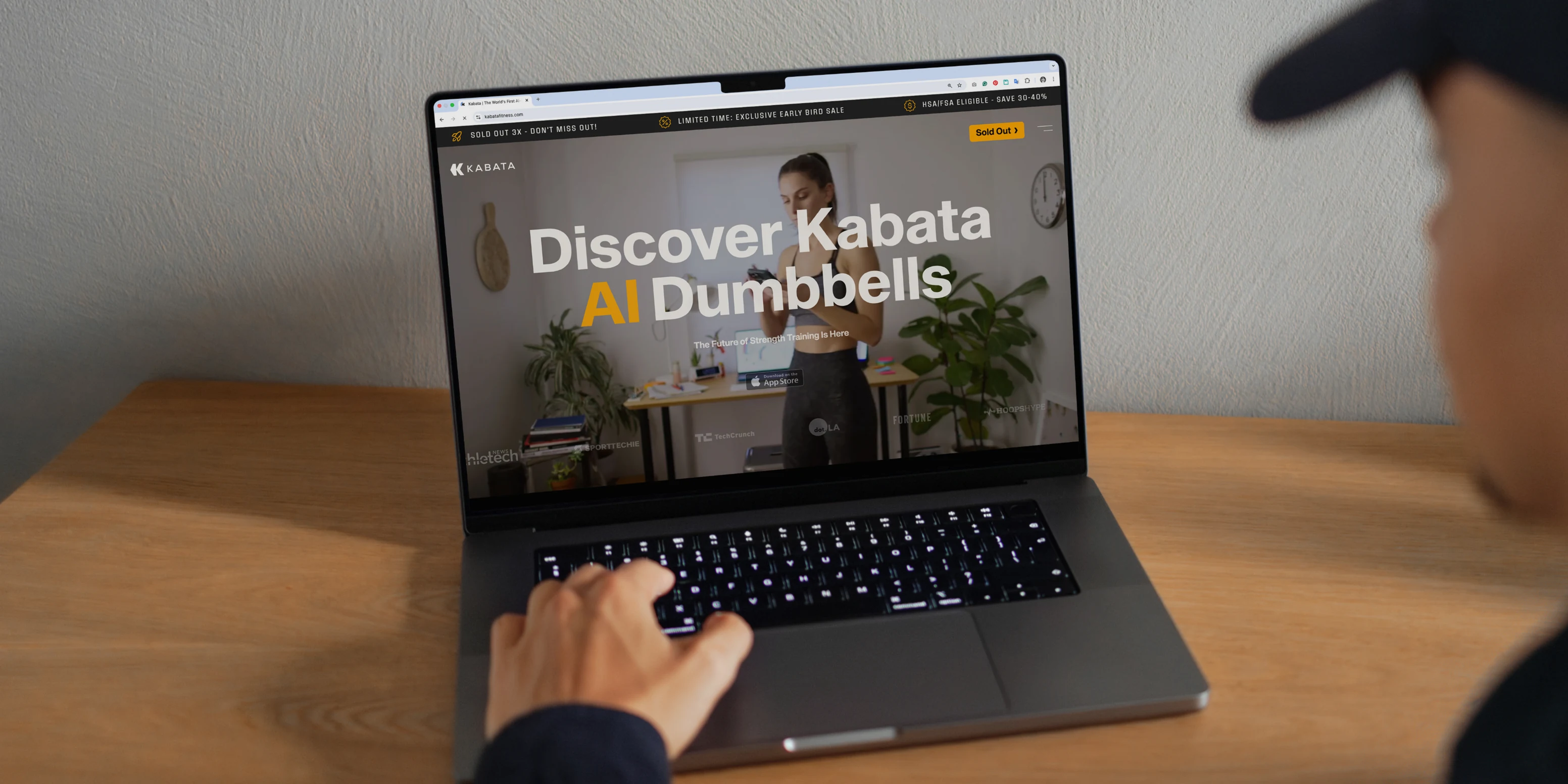 A laptop on a wooden desk showing the Kabata site, Discover Kabata AI Dumbbells across the top